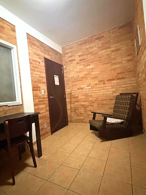 A room with a wooden brick wall, a dark door, a window, a dining table with chairs, and a single armchair. - Pousada Siloé (Vinhedo)