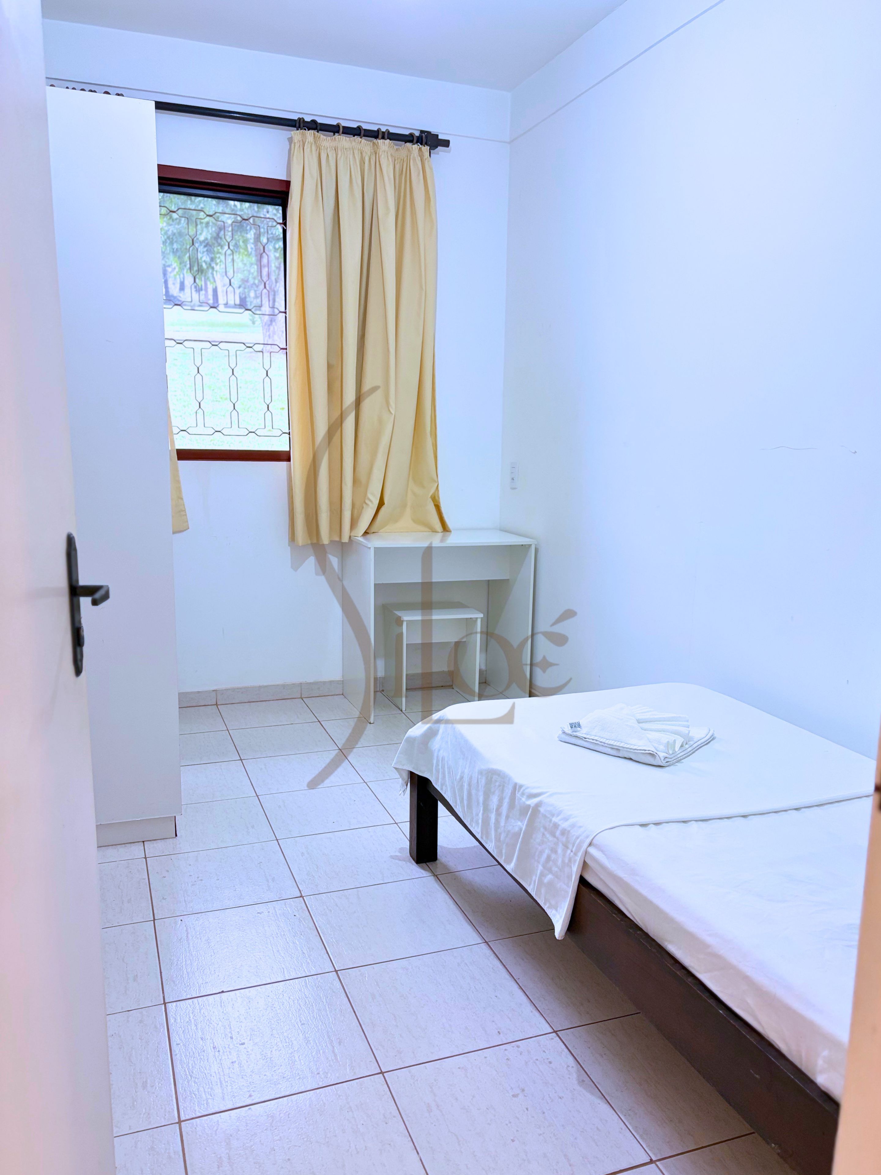 A small, clean room with a bed, a chair, and a window with curtains.