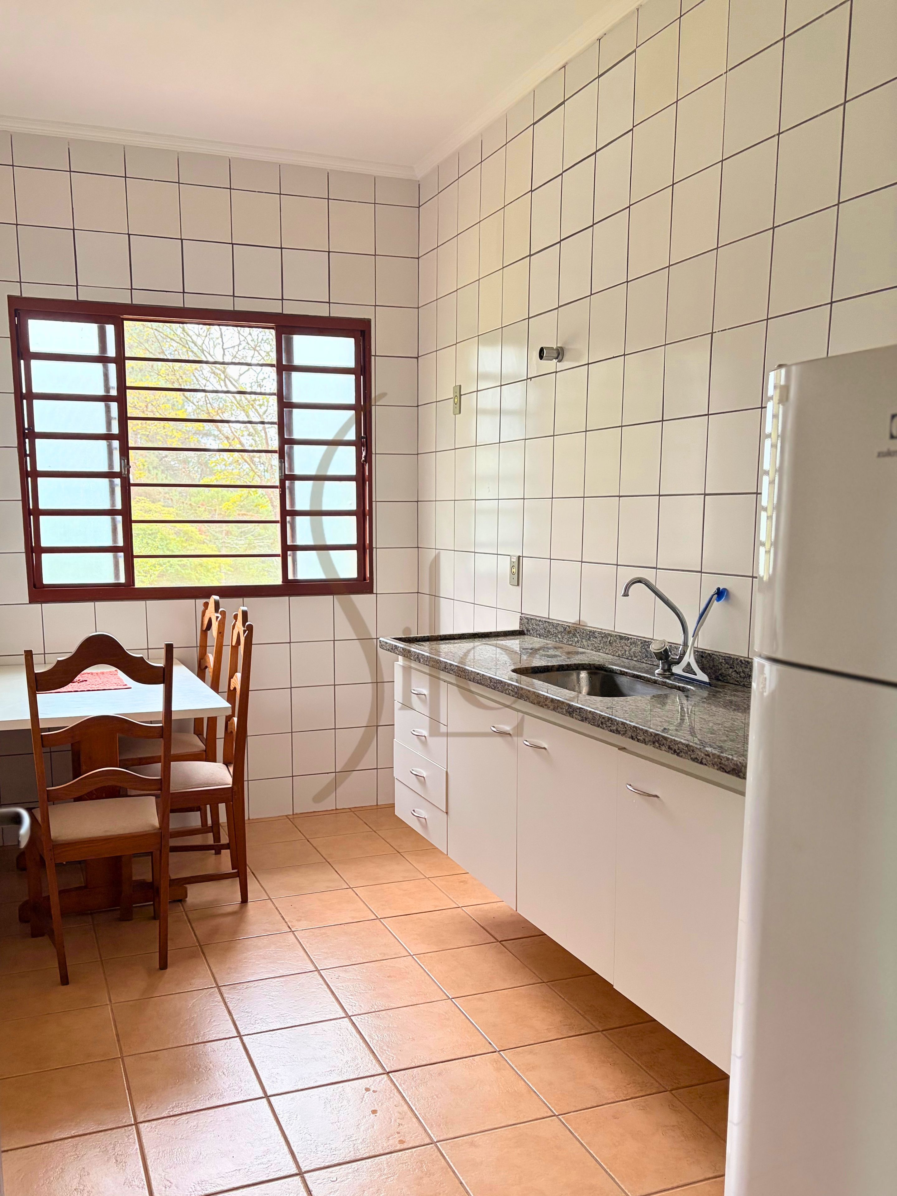 Cozinha com armários brancos, bancada de granito, pia e janela com vista para árvores.