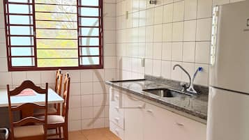 Cozinha com armários brancos, bancada de granito, pia e janela com vista para árvores.