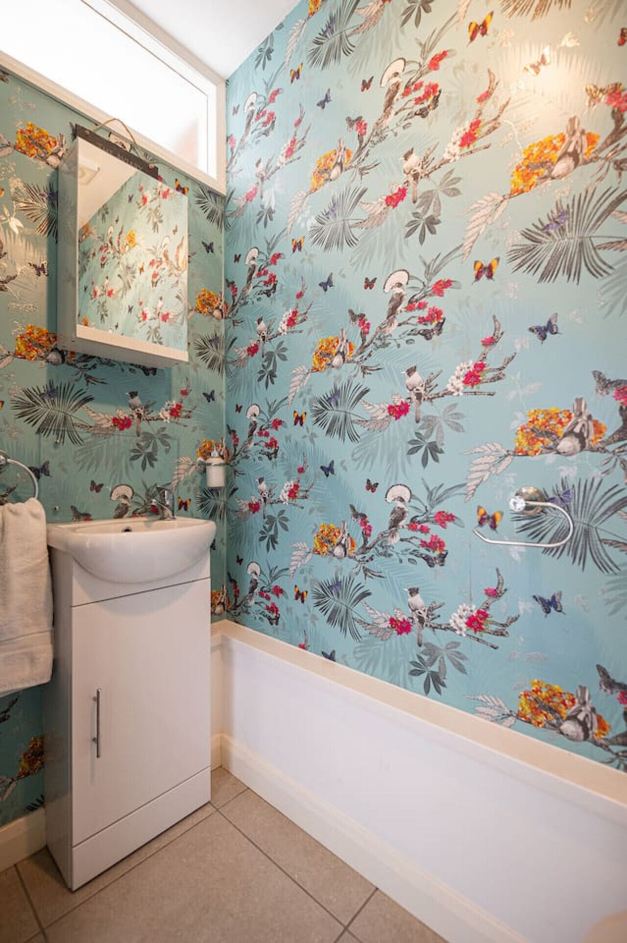 A bathroom with a floral wallpaper, a sink, and a mirror.