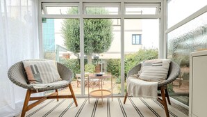 Ein Balkon mit zwei Korbstühlen, einem kleinen runden Tisch und Blick auf einen Garten und Gebäude.
