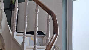 A staircase with white balusters and a wooden handrail, leading to a landing with a framed picture and a hanging plant.