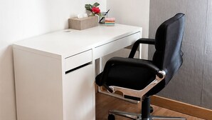 A white desk with a black office chair, a small plant, and a box of tissues.