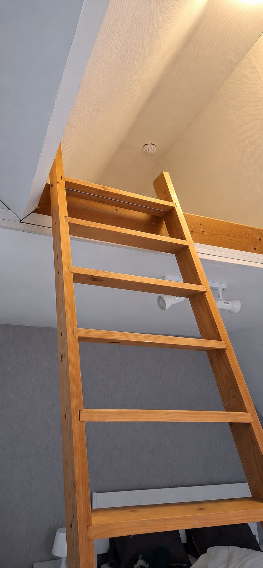 A wooden ladder in a room with a sloped ceiling and a ceiling light fixture.