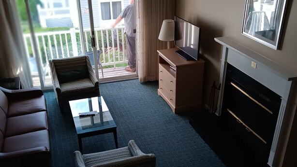 A hotel room with a balcony, a sofa set, a TV, a fireplace, and a lamp. - Cozy 2-bedroom condo with AC, fitness room in charming Westbrook. Oceanfront, (Westbrook)