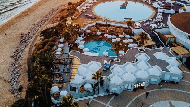 Vue aérienne d’un complexe hôtelier doté d’une piscine, d’un accès à la plage et de bâtiments blancs.