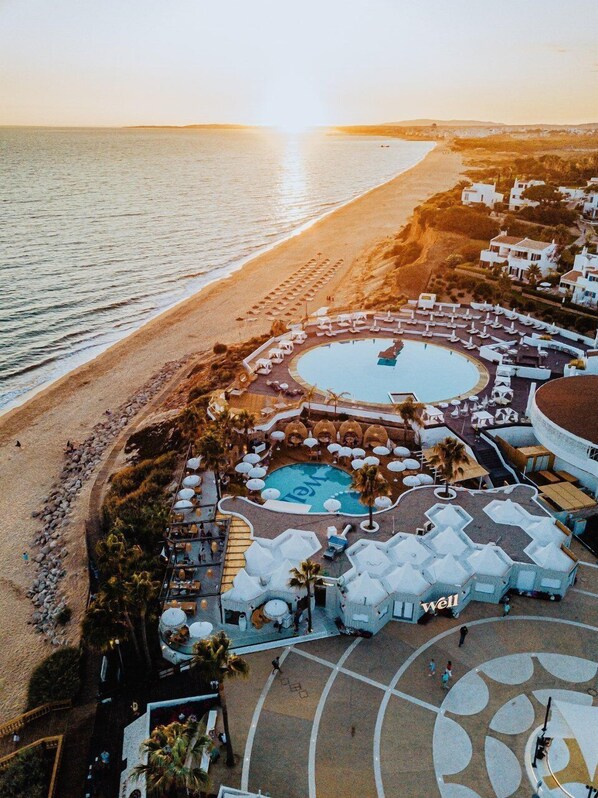 An aerial view of a resort with a swimming pool, beach access, and white buildings.