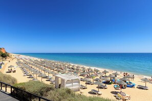 A beach with numerous sun loungers and umbrellas, a clear blue sky, and a calm sea.