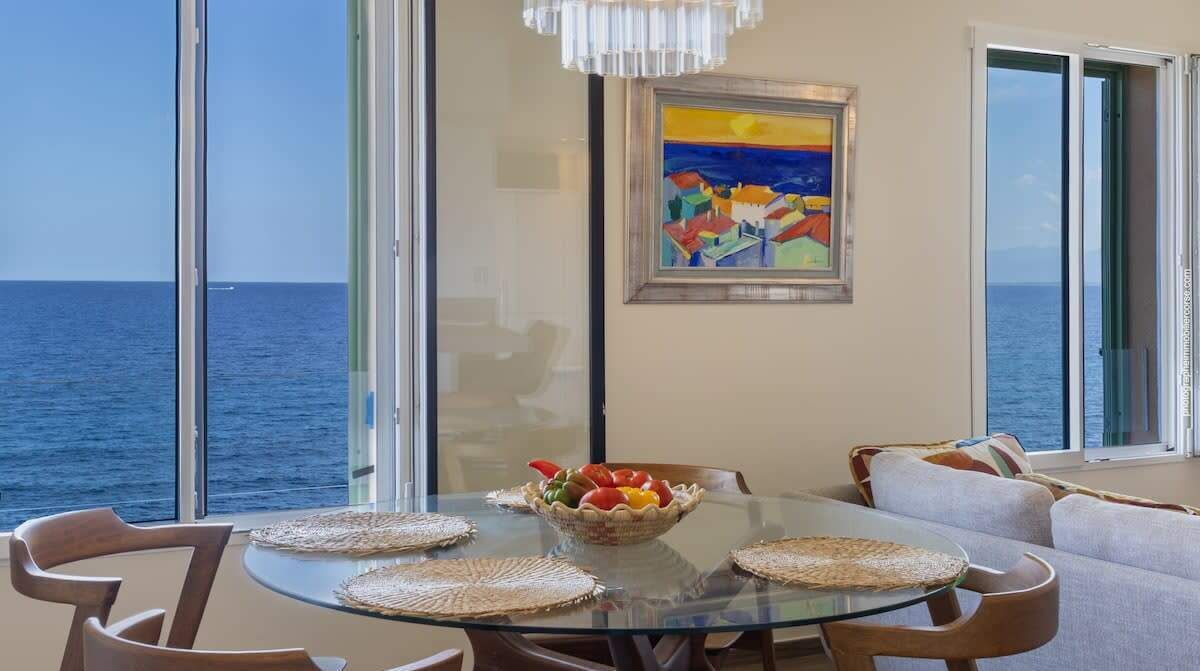A dining area with a glass table, wicker placemats, and a bowl of fruit.