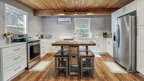 Een moderne keuken met witte kasten, roestvrijstalen apparatuur, een houten plafond en een centraal eiland met barkrukken.