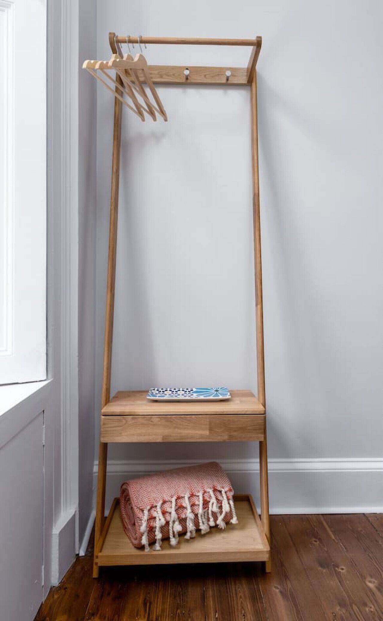 A wooden floor-to-ceiling storage unit with a shelf and a hanging rack.