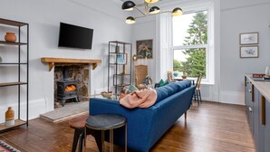 A living room with a fireplace, a sofa, a coffee table, and a TV mounted on the wall. - Stirling Retreat - Quirky Décor, Fireplace & Charm (Stirling)