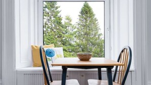 A dining area with a table and two chairs, a window with a view of trees, and a bench with cushions. - Stirling Retreat - Quirky Décor, Fireplace & Charm (Stirling)