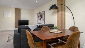 A modern living room with a sofa, a dining table with chairs, a TV, and a floor lamp. - Stirling's Hidden & Tranquil Studio Apartment (Stirling)