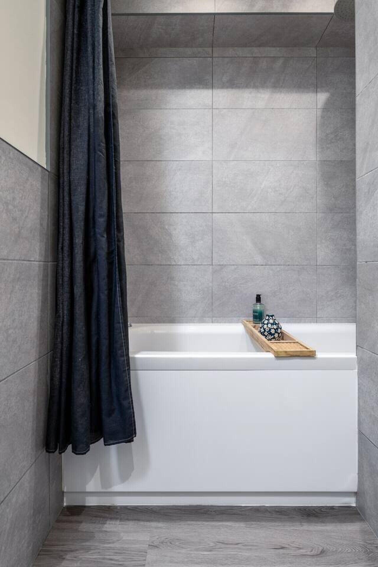 Un bagno con una vasca, un vassoio di legno con articoli da toilette e una tenda scura.