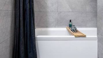 Un bagno con una vasca, un vassoio di legno con articoli da toilette e una tenda scura.