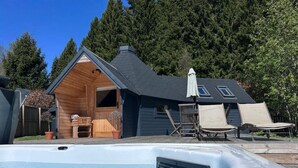 Un jacuzzi, terraza de madera, sillas de descanso y una casa con techo inclinado.