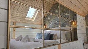Un dormitorio con un espejo grande que refleja una cama, almohadas y un tragaluz.
