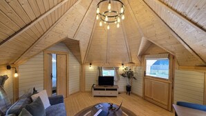 Una habitación acogedora en el ático con techo de madera, televisión, sofá, mesa de comedor y ventana con vistas.