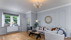 A spacious living room with a wooden floor, a grey sofa, a coffee table, and a chandelier.