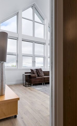 A room with large windows, a brown sofa, a wooden table, and a lamp. - The Stirling Penthouse - Free Parking (Stirling)