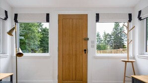 A room with a wooden door, two windows with blinds, a standing lamp, a wooden chair, and a small table. - Craighall House, Stunning River Tay Views & Garden (Stanley)