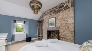 A bedroom with a stone wall, a fireplace, a window, and a bed with white bedding. - Craighall House, Stunning River Tay Views & Garden (Stanley)