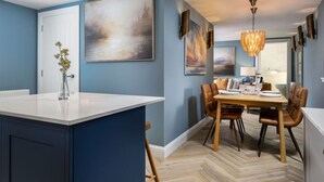 A modern kitchen with a central island, blue walls, and a dining area with a chandelier. - Craighall House, Stunning River Tay Views & Garden (Stanley)