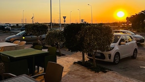 A parking area with a sunset view, outdoor seating, and a white car parked near the entrance.