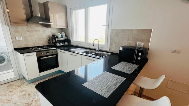 A modern kitchen with a black countertop, white cabinets, a built-in oven, and a window above the sink.