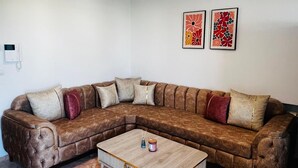 A living room with a brown leather sectional sofa, a wooden coffee table, and two framed artworks on the wall.