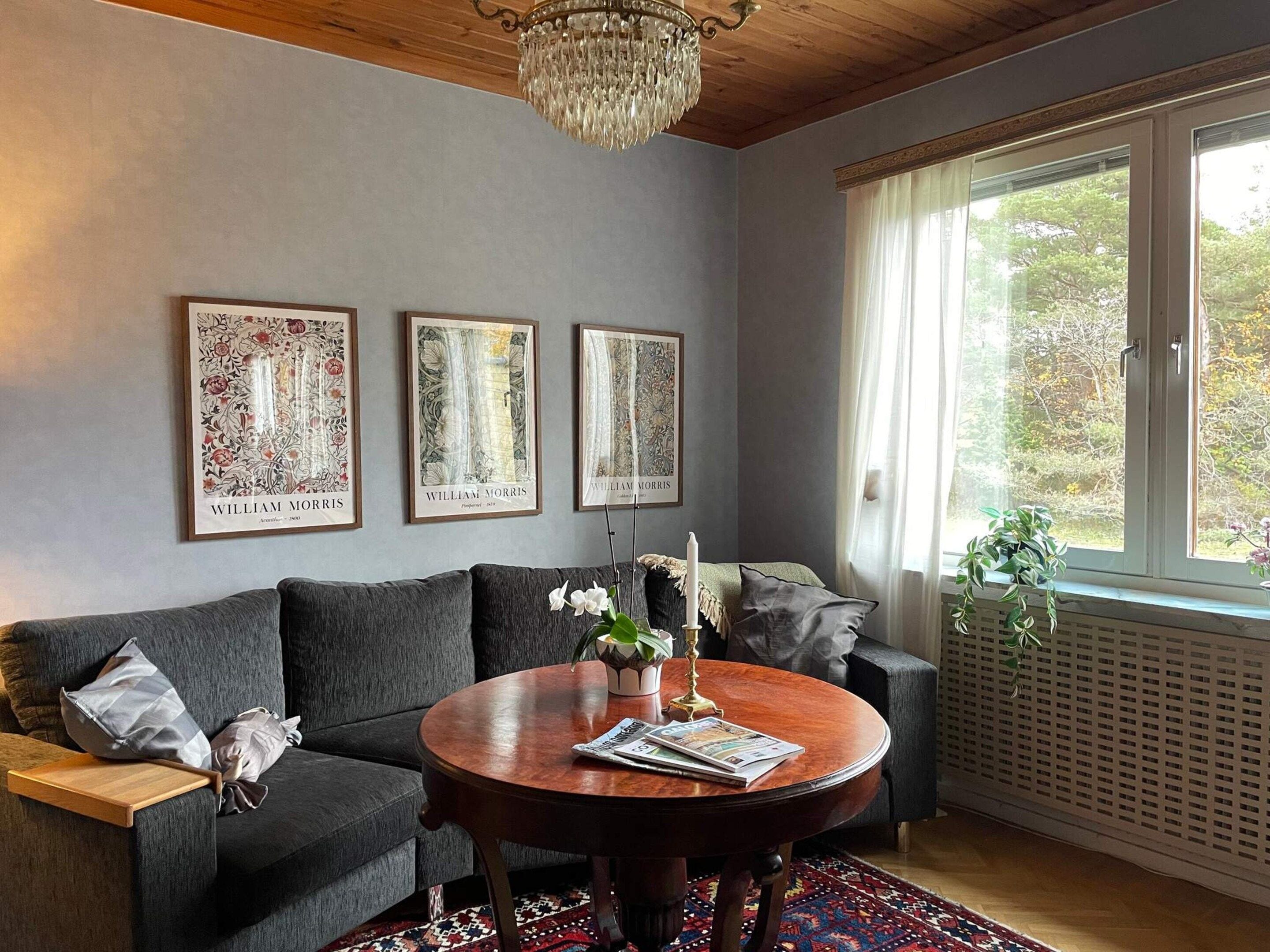 A cozy living room with a dark grey sofa, a round wooden coffee table, and three framed botanical prints on the wall.