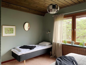 A room with a single bed, a bedside table, a window with curtains, a wall-mounted mirror, and a framed picture. - 4 Star Holiday Home in Visby (Visby)