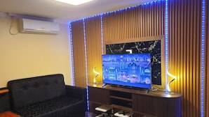 A modern living room with a flat-screen TV, dark sofas, and a wooden accent wall.