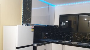 A modern kitchen with white cabinets, a black countertop, and blue LED strip lighting.