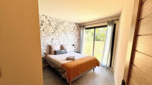 Een slaapkamer met een bed, een nachtkastje, een raam met gordijnen en uitzicht op het omliggende landschap.