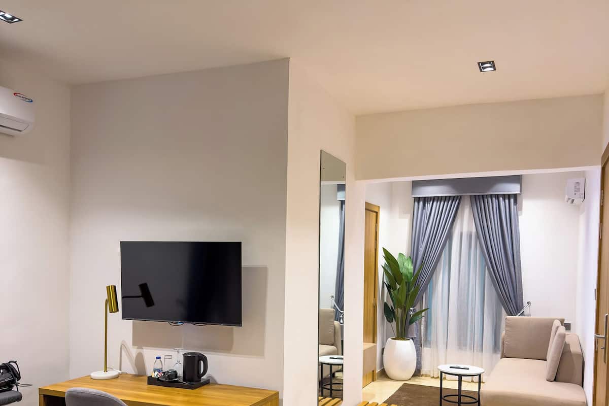 Ein modernes Hotelzimmer mit Holzschreibtisch, Flachbildfernseher, Sofa, Couchtisch und einer Topfpflanze.