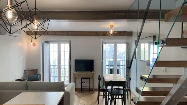 A modern living room with a dining area, wooden floors, a TV, and a staircase.