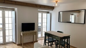 A modern living room with a TV, wooden dining table, chairs, and a large mirror.