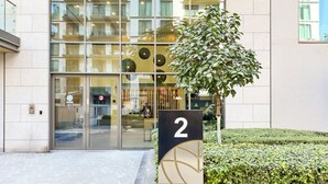 A modern building with a glass facade, a number 2 sign, and a well-maintained hedge. - PVH - Serene 2BR - Sobha Hartland Greens (Dubai)