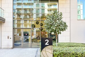 A modern building with a glass facade, a number 2 sign, and a well-maintained hedge. - PVH - Serene 2BR - Sobha Hartland Greens (Dubai)