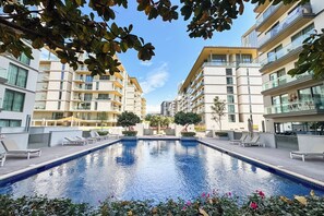 En swimmingpool omgivet af moderne bygninger med altaner og en klar himmel.