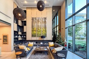 A modern living room with a large window, a fireplace, and a Christmas tree. - PVH - Serene 2BR - Sobha Hartland Greens (Dubai)