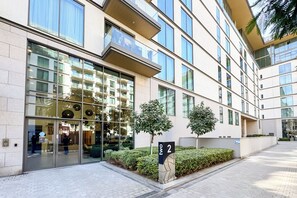 A modern building with large windows, a glass entrance, and a small tree in the foreground. - PVH - Serene 2BR - Sobha Hartland Greens (Dubai)