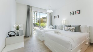 A modern hotel room with a large window, two beds, a desk, and a small plant. - PVH - Serene 2BR - Sobha Hartland Greens (Dubai)
