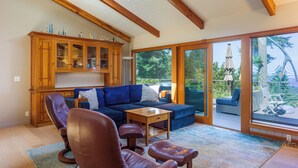 Un vaste salon agrémenté d’un meuble en bois, de fauteuils en cuir, d’un canapé bleu et offrant une vue sur l’extérieur grâce à de grandes portes-fenêtres coulissantes.