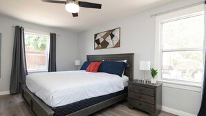 A bedroom with a bed, nightstands, a ceiling fan, a window with curtains, and a wall art piece.