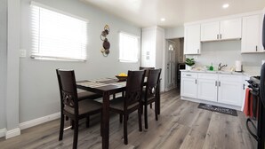 A modern kitchen with white cabinets, a dining area with a wooden table and chairs, and a black and white rug.