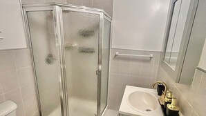 Un baño con cabina de ducha de vidrio, un inodoro y un lavabo con grifo dorado.